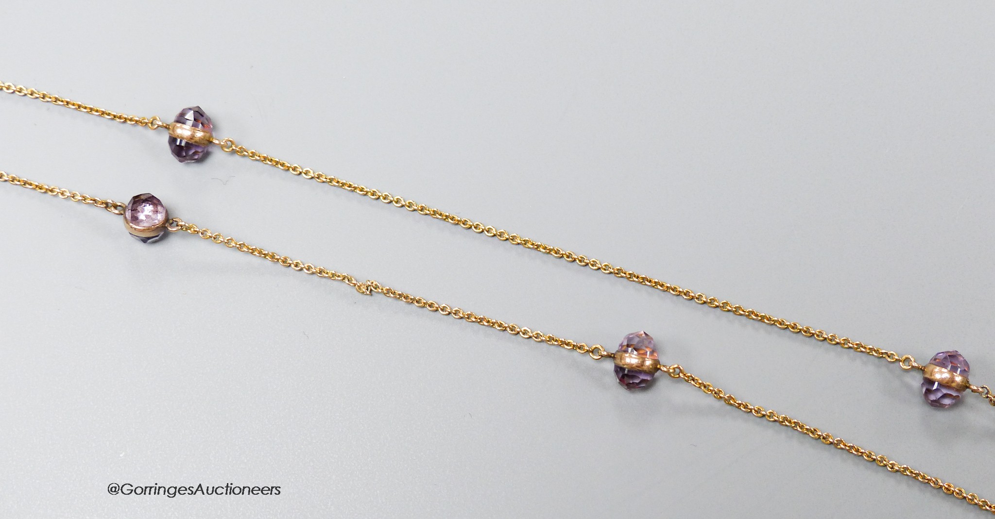 A yellow metal (stamped 14k) and facet cut purple stone set guard chain, 98cm, (link has become detached), gross weight 11.7 grams.